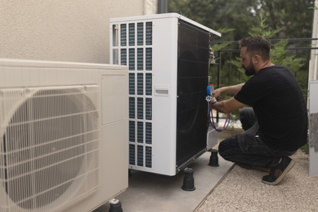 The man installs and adjusts the heat pump in the yard. T